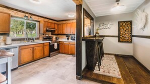 A kitchen with wooden cabinets, a countertop, a sink, and a bar area with stools. - Harrisonburg 3 bedroom and HOT TUB! Minutes from Downtown NEW! (Harrisonburg)