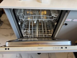 An open dishwasher with a control panel, a metal rack, and a tiled floor.