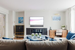 Ein Wohnzimmer mit einer Couch, einem an der Wand montierten Fernseher, einem Schrank und einem Tisch mit Blumen.