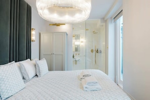 Ein modernes Hotelzimmer mit einem großen Bett, einer Glaskabinent Dusche und einem Kronleuchter.