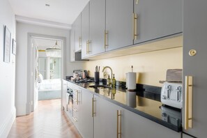 Eine moderne Küche mit grauen Schränken, goldenen Griffen und einer schwarzen Arbeitsplatte.