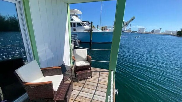 Ein Bootsdeck mit Korbstühlen, einem Tisch und Blick auf das Wasser sowie ein weiteres Boot.