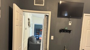 Ein Zimmer mit einer zur Diele hin gehenden Tür, einem wandmontierten Fernseher, einem Wandregal und einer Vase.