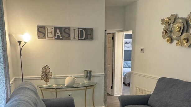 Ein Wohnzimmer mit zwei grauen Sofas, einem Glastisch, einem an der Wand befestigten Schild mit der Aufschrift 'SEASIDE' und einer Wanddekoration.