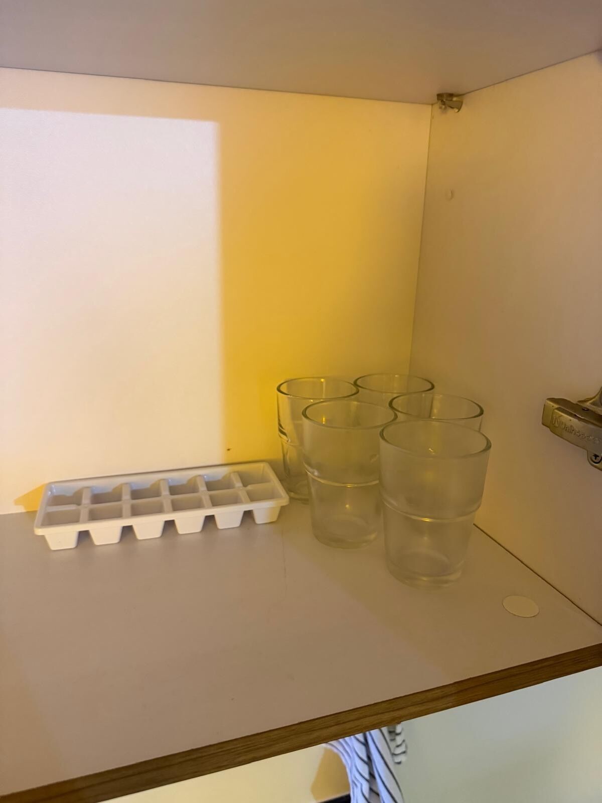 A white shelf with a white ice cube tray and four clear glasses.