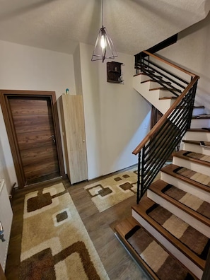 A staircase with wooden steps and a black metal railing, a wooden door, and a patterned rug on the floor.