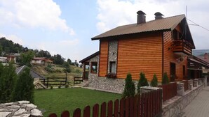 Una baita in legno con facciata in pietra, un cortile recintato e cielo sereno.