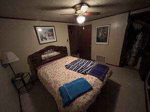 A bedroom with a bed, a ceiling fan, a lamp, and framed pictures on the wall.