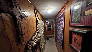 A hallway with wooden walls, a zebra wall hanging, framed pictures, and a carpeted floor. - Quaint 2-bedroom house with AC in charming Karnack (Karnack)