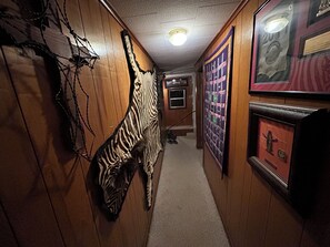 A hallway with wooden walls, a zebra wall hanging, framed pictures, and a carpeted floor. - Quaint 2-bedroom house with AC in charming Karnack (Karnack)