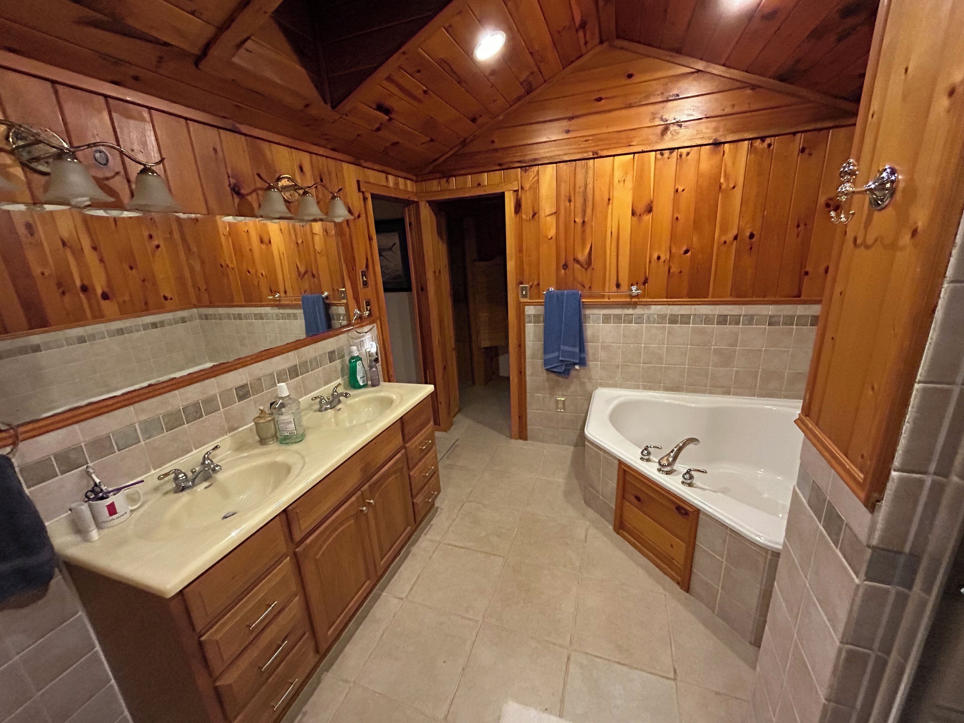 Een badkamer met houten lambrisering, twee wasbakken, een bad en een spiegel.