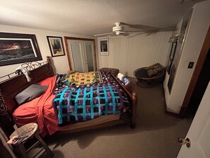 A bedroom with a bed, a chair, a ceiling fan, and a door.