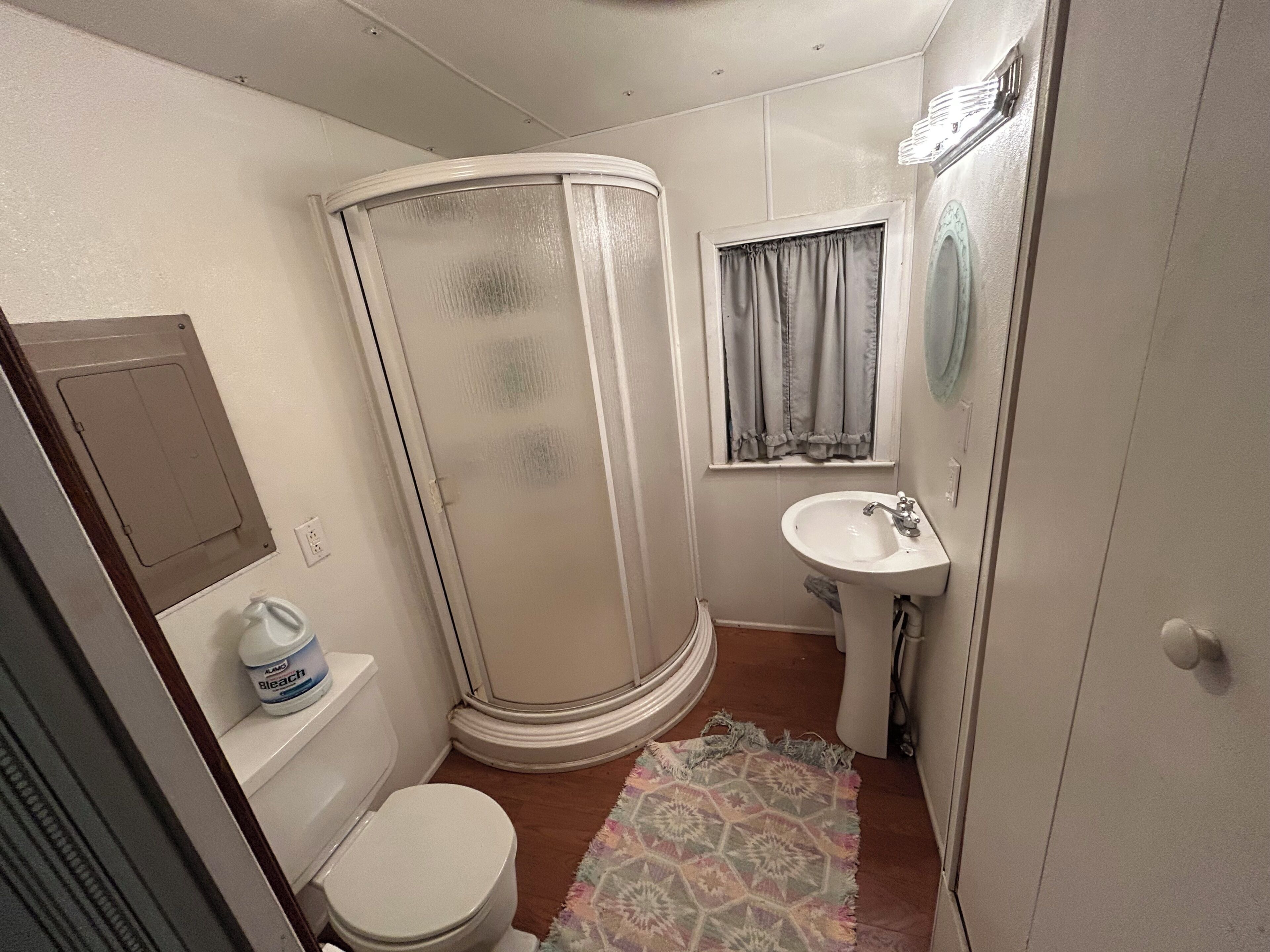 Een kleine badkamer met toilet, douchecabine, wastafel en een raam met gordijnen.