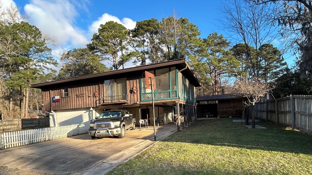 A two-story house with a garage, a white picket fence, and a grassy yard. - Quaint 2-bedroom house with AC in charming Karnack (Karnack)