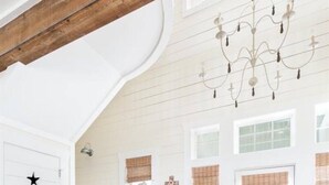 Una habitación amplia con una escalera de madera, un candelabro y un ventanal con persianas.
