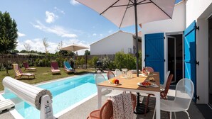 A backyard with a swimming pool, lounge chairs, a table with food, and a blue door. - Luxury 8-person Private Pool Villa (Les Sables-d'Olonne)