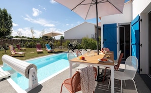 A backyard with a swimming pool, lounge chairs, a table with food, and a blue door. - Luxury 8-person Private Pool Villa (Les Sables-d'Olonne)