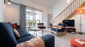 A modern living room with a sofa, armchair, TV stand, and a staircase. - Luxury 8-person Private Pool Villa (Les Sables-d'Olonne)