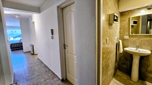 A hotel hallway with a door, a telephone, and a bathroom with a sink and mirror. - Refugio Urbano  Bariloche (San Carlos de Bariloche)