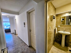 Corredor de hotel com porta, telefone e banheiro com pia e espelho.
