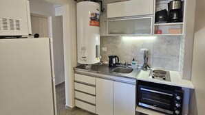 A compact kitchen with a refrigerator, microwave, stove, and a water heater. - Refugio Urbano  Bariloche (San Carlos de Bariloche)