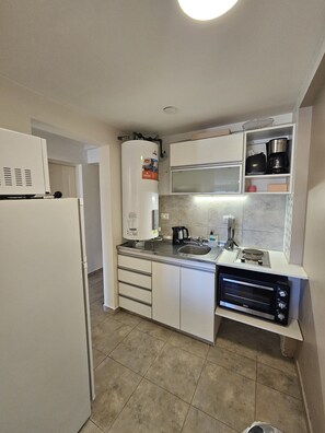 Cozinha compacta com geladeira, micro-ondas, fogão e aquecedor a água.