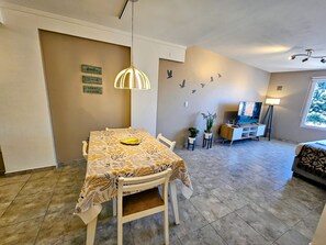 Uma área de refeições com mesa, cadeiras, luminária pendente, televisão e janela.