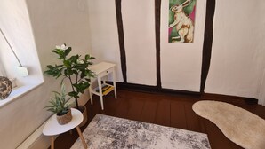 A room with a white wall, a painting of a rabbit, a small white table, a potted plant, and a white rug. - Baroque-Era Vacation Home (Neumagen-Dhron)