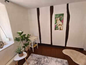 Ein Zimmer mit weißer Wand, einem Hasenbild, einem kleinen weißen Tisch, einer Topfpflanze und einem weißen Teppich.