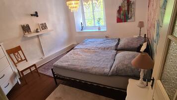 Um quarto com cama, janela, lustre, abajur e um quadro.
