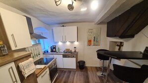 A compact kitchen with white cabinets, a wooden countertop, a stove, a sink, and a small dining area with a black chair. - Baroque-Era Vacation Home (Neumagen-Dhron)