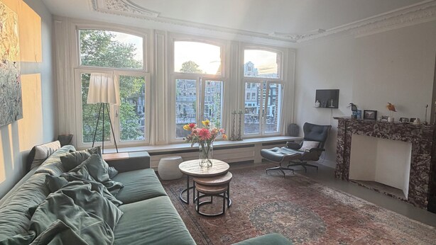 Un salon avec un canapé, une table ronde ornée d’un vase, un fauteuil et une cheminée.