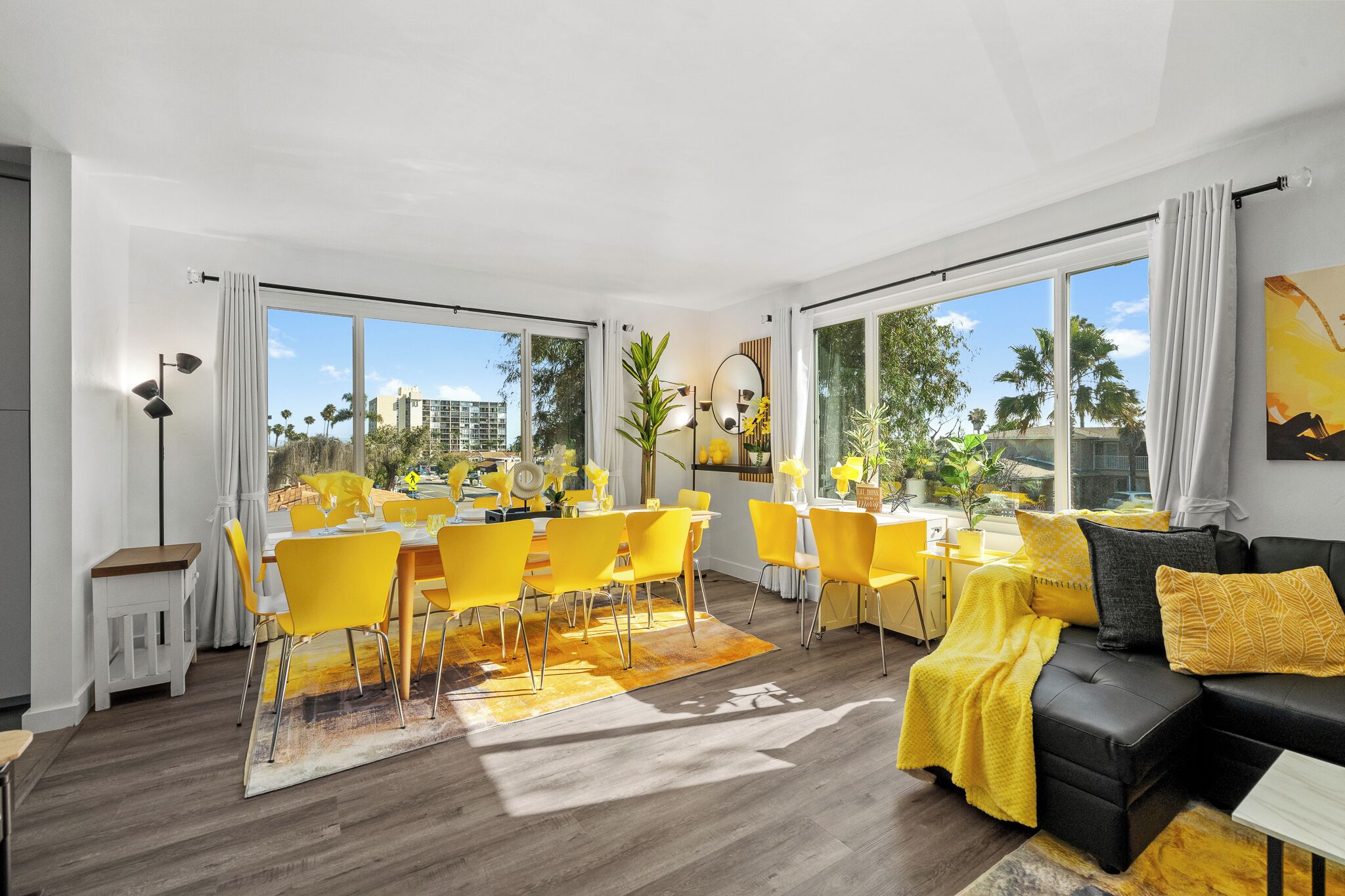 Un salon moderne comprenant un coin repas, de grandes fenêtres et un canapé noir agrémenté de coussins jaunes.
