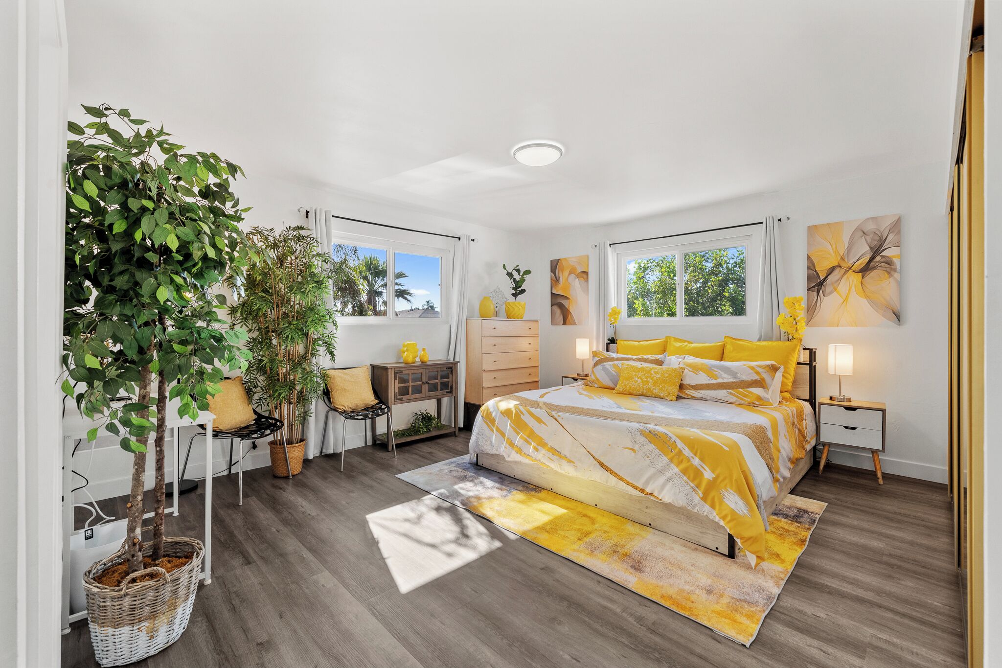 A bedroom with a bed, bedside tables, a dresser, a chair, a desk, a potted plant, and a window.