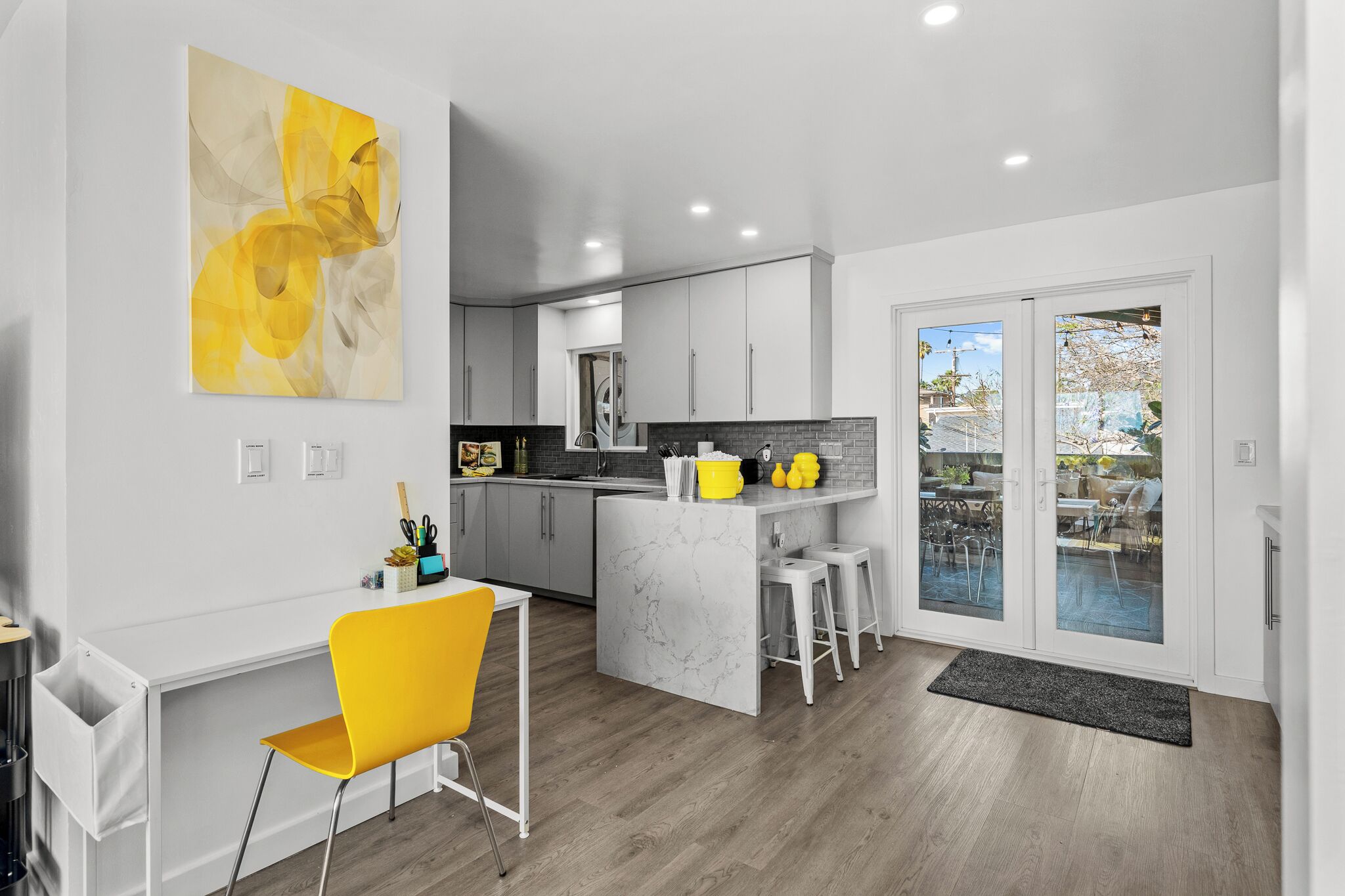 A modern kitchen with a marble island, a yellow chair, and a large window.