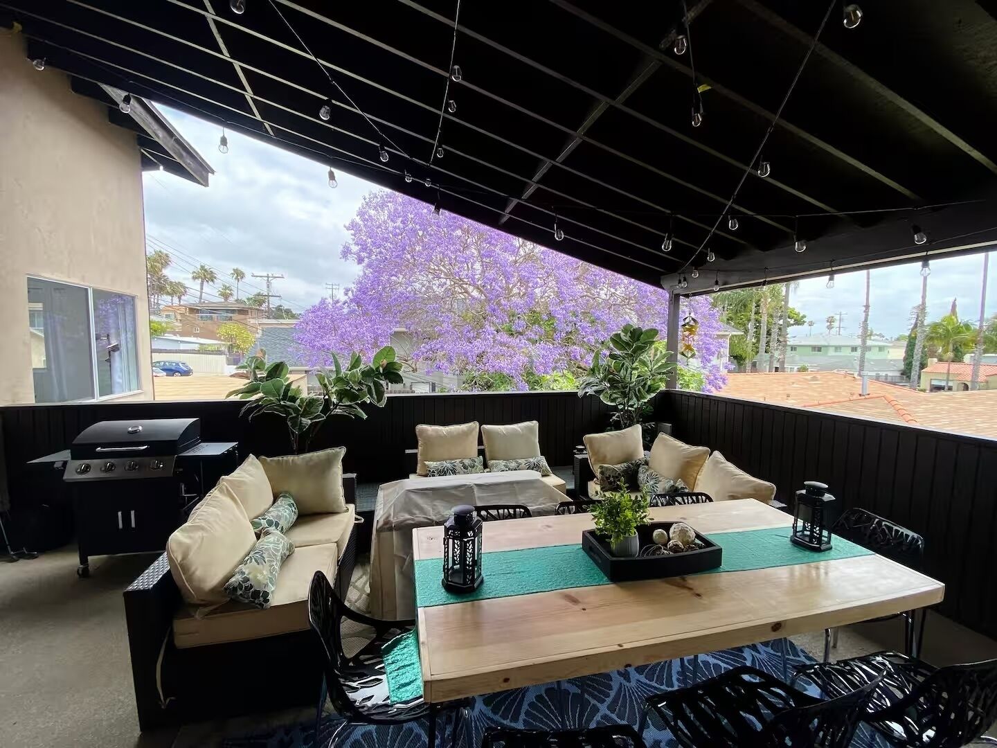 Eine Terrasse im Freien mit einem Holztisch und Stühlen, einem Grill und Blumentöpfen.