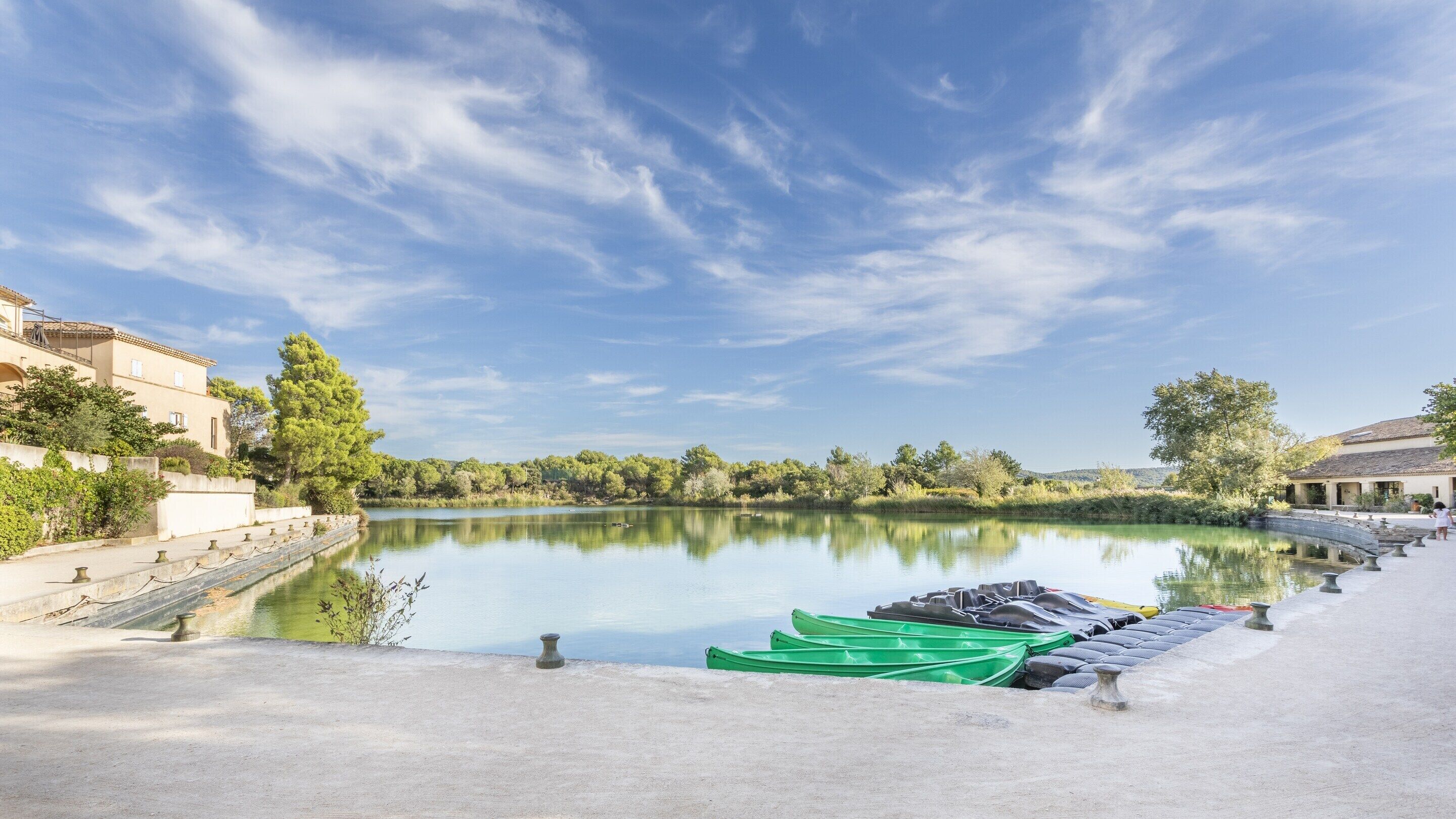 A calm lake with boats, a clear sky, and buildings on the shore.