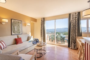 A living room with a sofa, a small table, and chairs, a balcony with a view, and a dining area with a counter. - Chic Countryside Stay With Balcony (Mallemort)