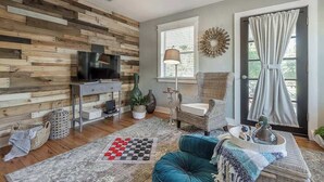 Un salon avec un mur en bois, un téléviseur, un canapé, une table basse et une fenêtre avec des rideaux.