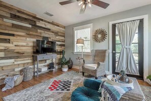 Ein Wohnzimmer mit einer Holzwand, einem Fernseher, einem Sofa, einem Couchtisch und einem Fenster mit Vorhängen.