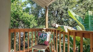 Une terrasse en bois avec une chaise et un coussin, entourée d’une végétation luxuriante et d’arbres.