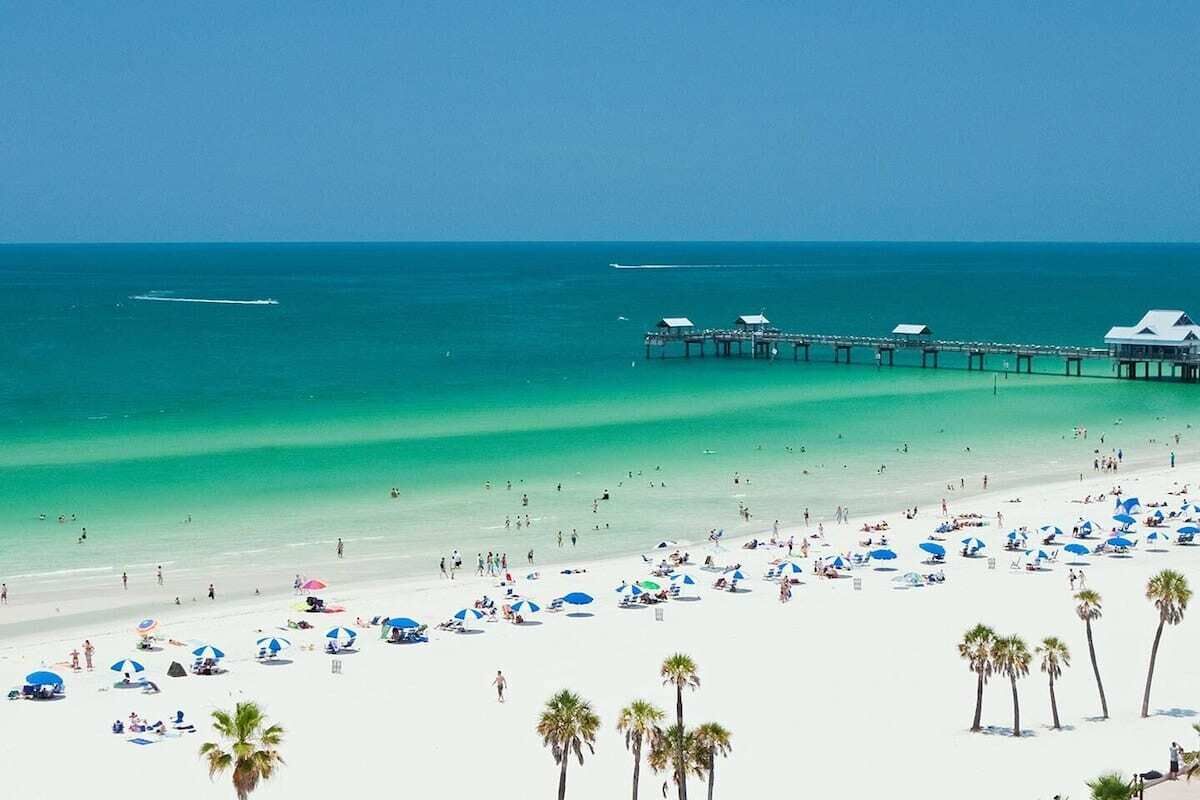 A beach with a pier extending into the ocean, white sand, and palm trees.