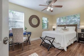 Ein Schlafzimmer mit Bett, Schreibtisch, Stuhl, Deckenventilator und einem Fenster mit Jalousien.