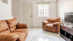 A living room with a brown sofa, a brown armchair, a flat-screen TV, and a white door. - Serene 2-bedroom house with AC in Puerto Vallarta great location. (Puerto Vallarta)
