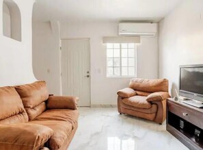 Ein Wohnzimmer mit braunem Sofa, einem braunen Sessel, einem Flachbildfernseher und einer weißen Tür.