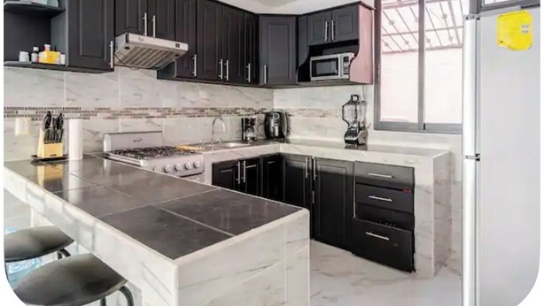 A modern kitchen with dark cabinets, a white countertop, a stove, and a refrigerator. - Serene 2-bedroom house with AC in Puerto Vallarta great location. (Puerto Vallarta)