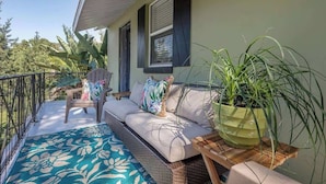 Un balcon agrémenté d’un canapé en osier, d’une chaise, d’une plante en pot et d’un tapis à motifs.