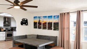 Una zona pranzo con tavolo e panche in legno, una cucina con elettrodomestici moderni e una ventola a soffitto.