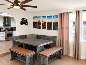 Ein Essbereich mit Holztisch und Bänken, eine Küche mit modernen Geräten und ein Deckenventilator.