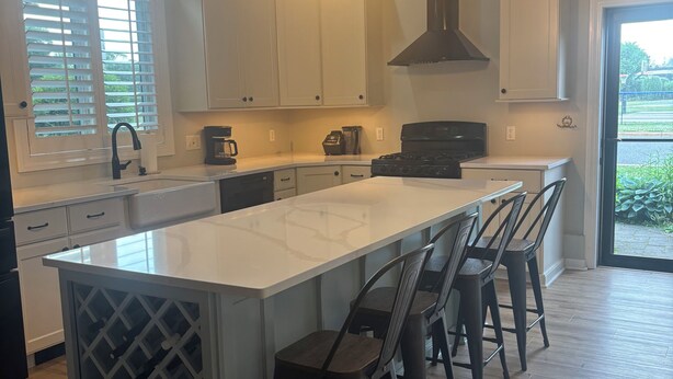 Een moderne keuken met een centraal eiland, barstoelen, een inbouw wijnkoeler en een groot raam met jaloezieën.